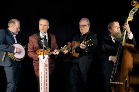 Neljä miestä instrumenttien kanssa. Vasemmalta katsoen banjo, mandoliini, kitara ja kontrabasso