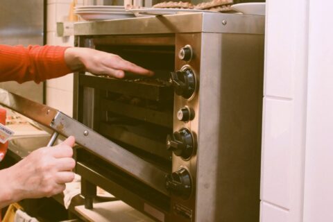 Käsi kurottaa kohti uunia, jossa on paistumassa karjalanpiirakoita